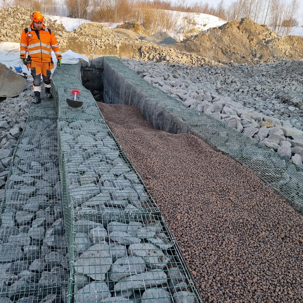 Uppbyggnad av filterdamm med olika materiallager, inklusive lättklinker, under anläggningsarbete.