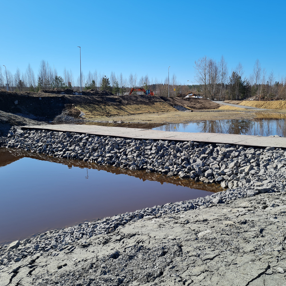Anlagd damm för dagvattenhantering med stenbeklädda slänter och reglerad vattennivå.