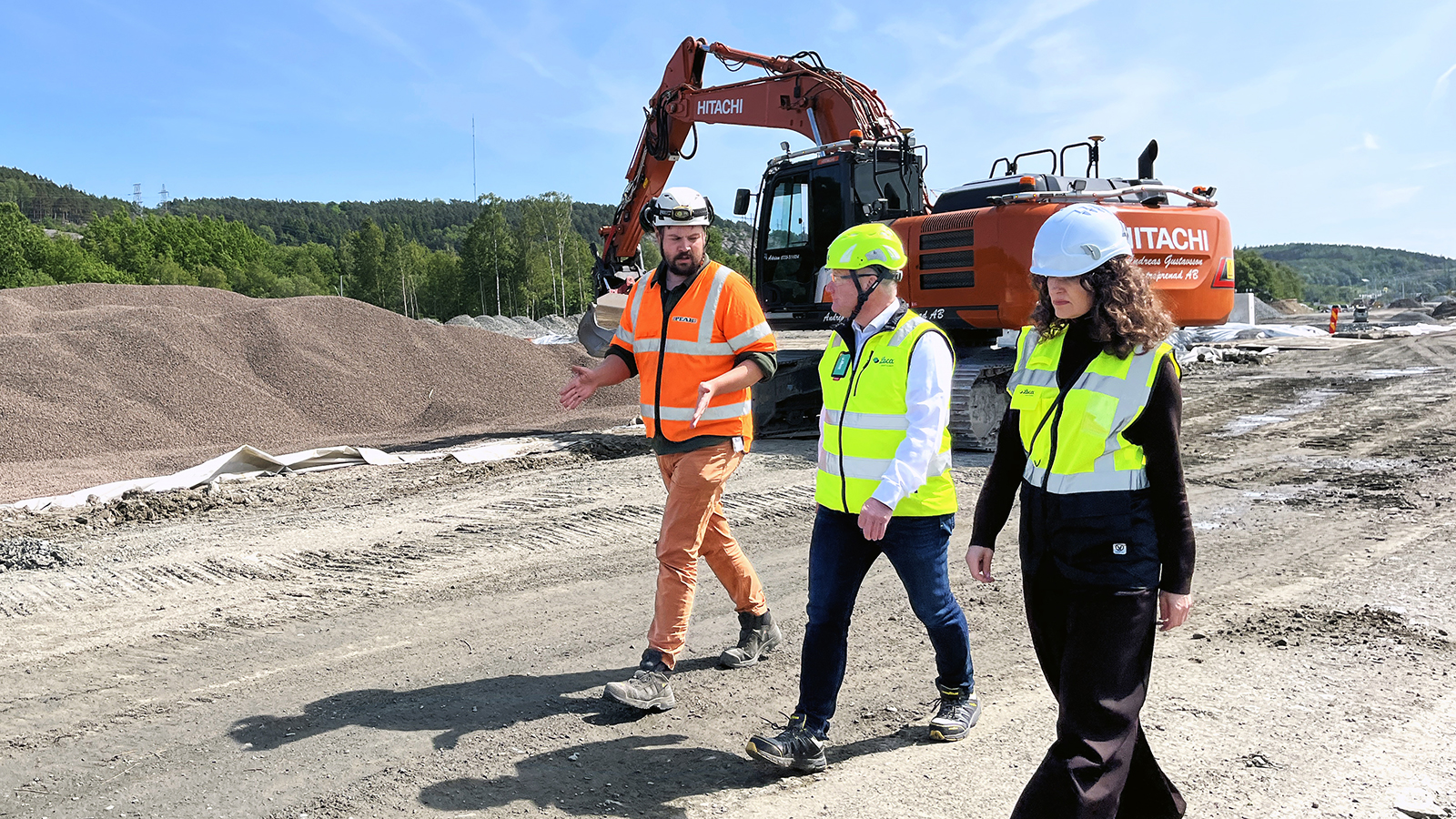 Platsbesök på byggarbetsplats med entreprenör och projektteam framför grävmaskin