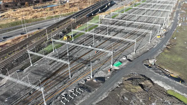 Flygfoto över pågående byggnation av Lärje uppställningsspår med flera parallella spår, kontaktledningsstolpar och grusballast, intill vägar och markarbeten i ett öppet landskap.
