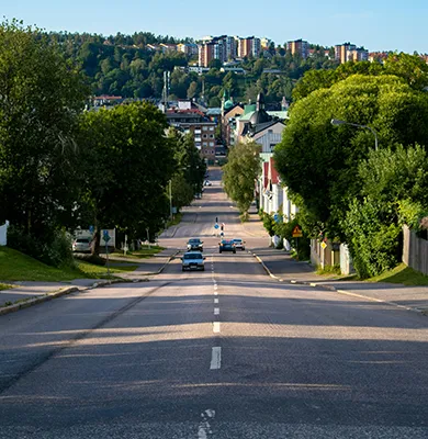 En bred stadsgata kantad av träd, med några bilar som kör i båda riktningarna. 
