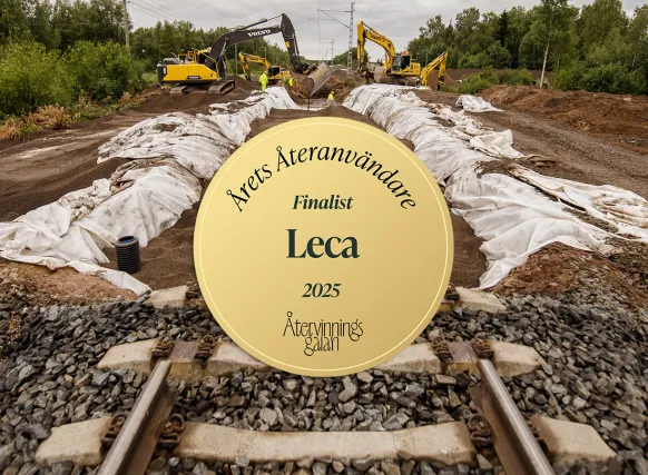Järnvägsarbete med flera grävmaskiner som lägger ut material längs spåret. I förgrunden syns en guldfärgad emblemsymbol med texten ”Årets Återanvändare – Finalist Leca 2025 – Återvinningsgalan”.