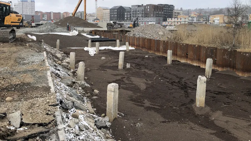 Byggarbetsplats med spontvägg och betongpålar där Leca Trans 2 lagts ut som lättfyllnad i schakt.