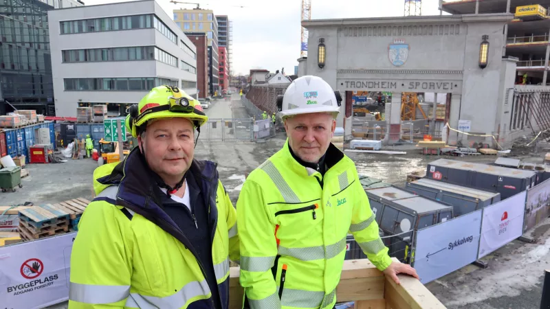 Två män från Leca Norge står med i hjälm och varseljacka framför en byggarbetsplats i Trondheim