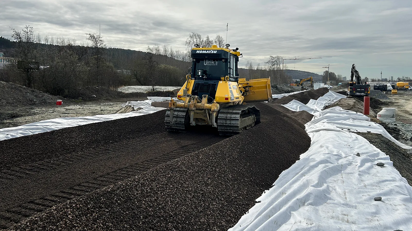 Bandtraktor fördelar återbrukad Leca lättklinker längs en vägsträcka under anläggningsarbete.
