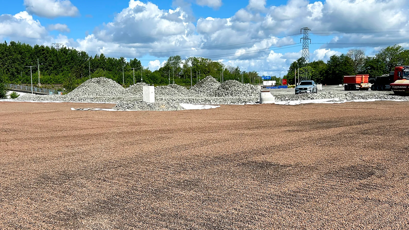 Utjämnad yta med återbrukad Leca lättklinker framför högar av krossmaterial och maskiner på en anläggningsplats.