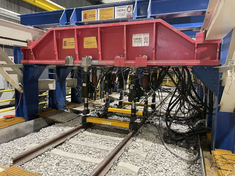 Tung laboratorieutrustning placerad ovanför spår för belastningstest av material.