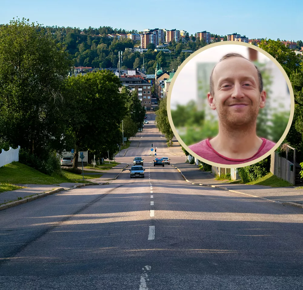 En bred stadsgata kantad av träd, med några bilar som kör i båda riktningarna. I förgrunden till höger syns ett infällt porträtt av en leende man med kort hår och röd t-shirt, mot en suddig grön bakgrund.