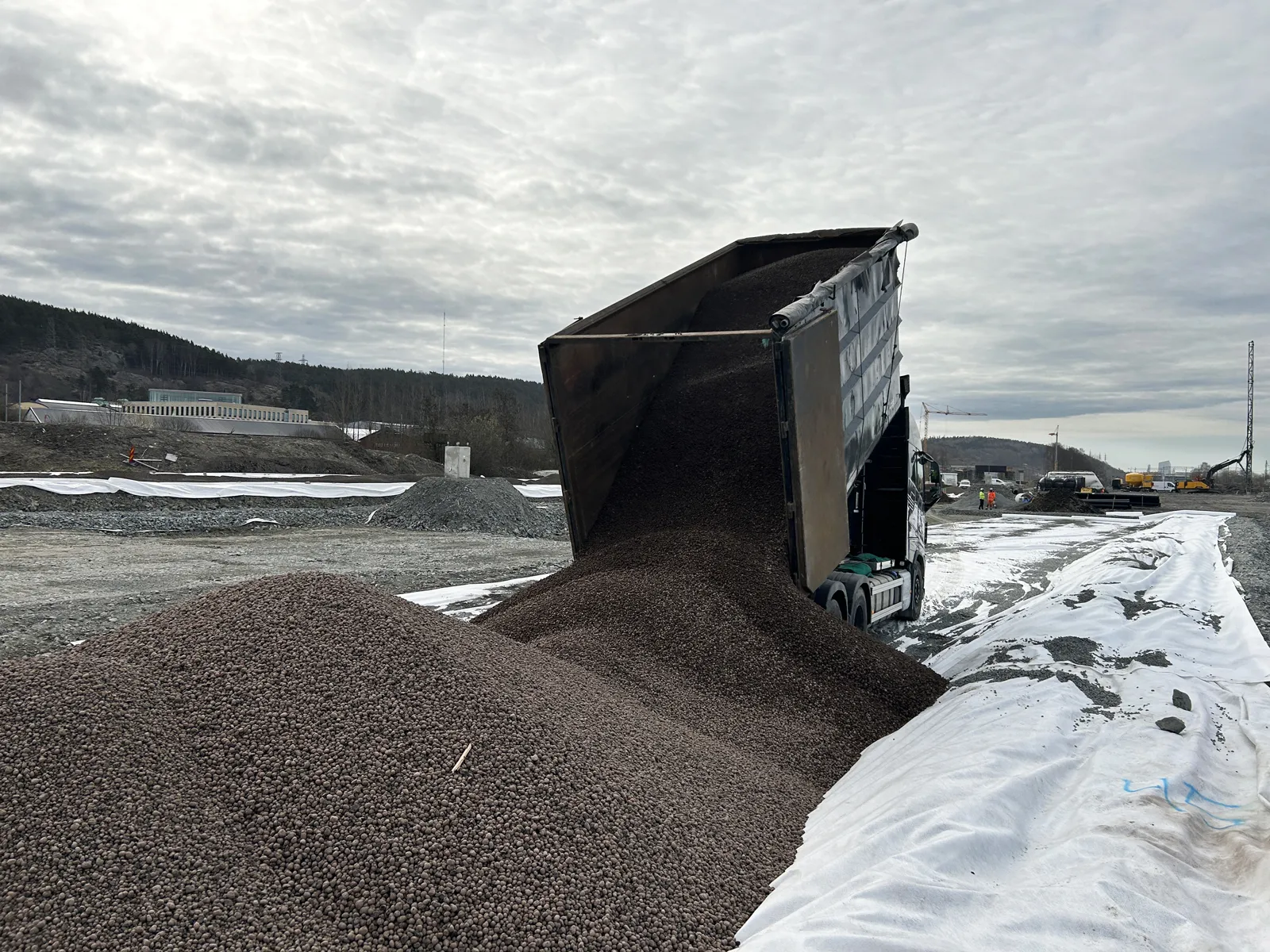 Lastbil tippar lättklinker ovanpå geotextil på byggarbetsplats i infrastrukturprojekt