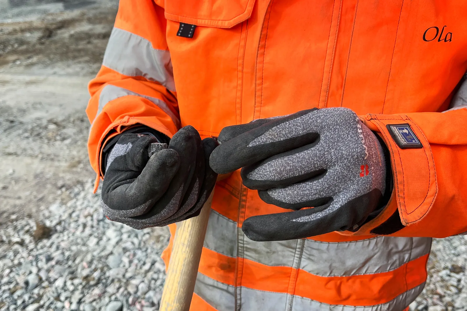 Närbild av person i orange varselkläder som håller lättklinker i handen på byggarbetsplats