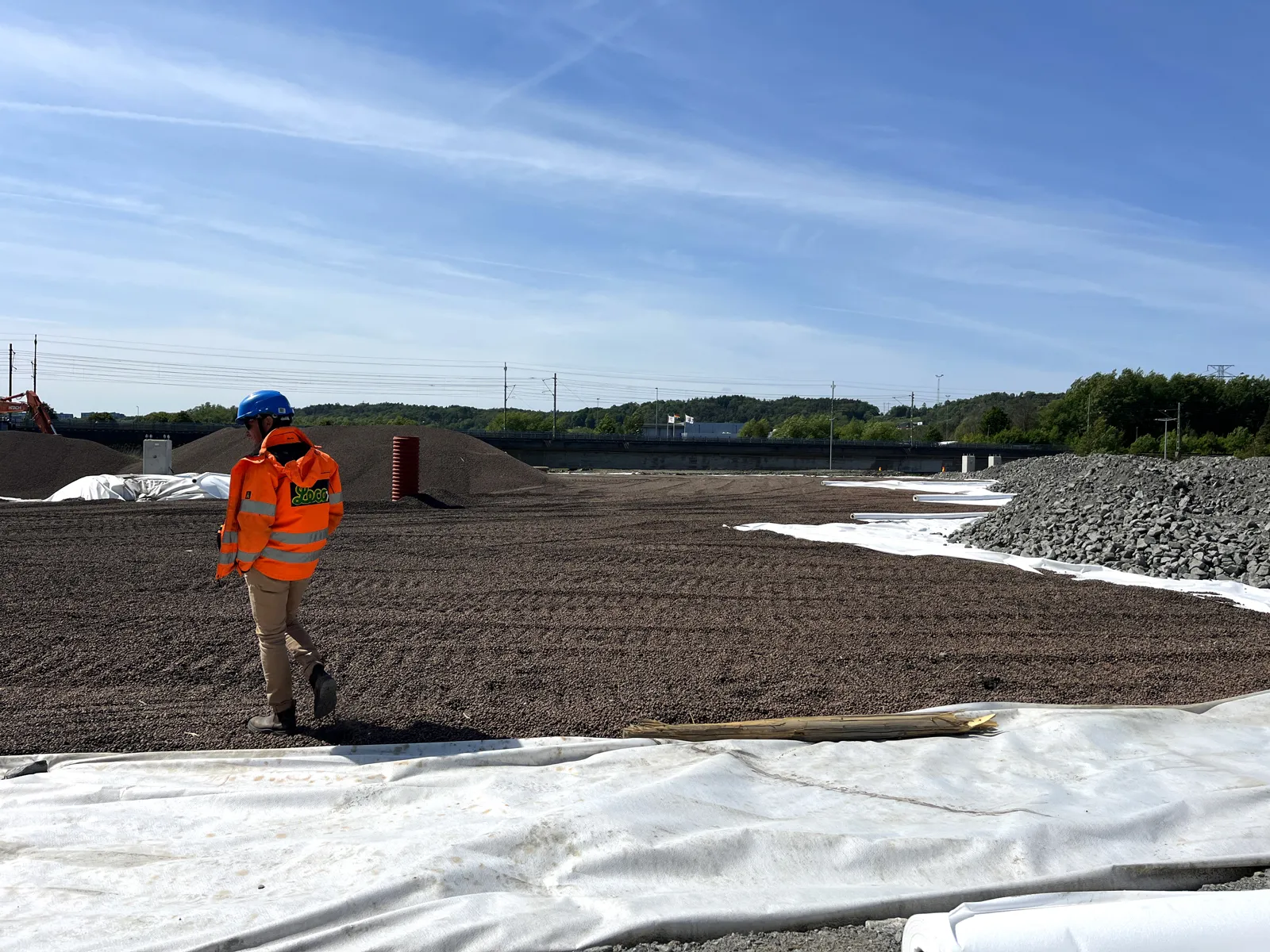 Arbete med lättklinker som lättfyllnad på byggarbetsplats, utlagd ovanpå geotextil i infrastrukturprojekt