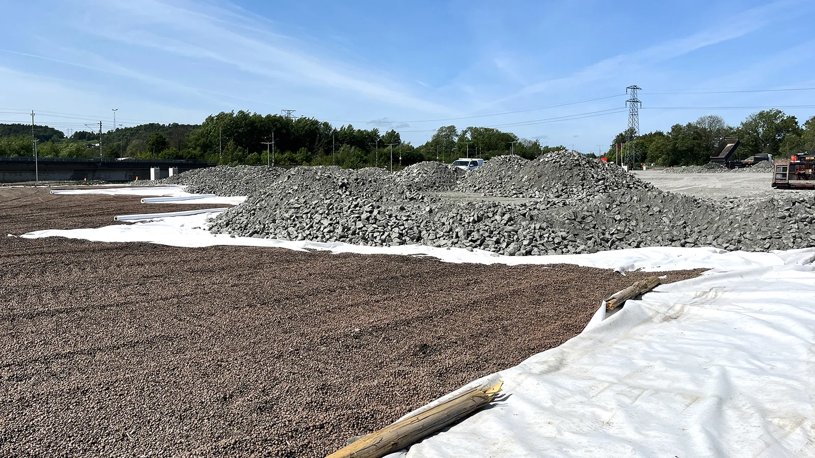Utlagd Leca lättklinker och fiberduk framför högar med krossmaterial på en anläggningsyta.