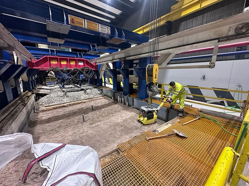 Arbetare använder vibroplatta för att packa underlag i testgrop i laboratoriemiljö.